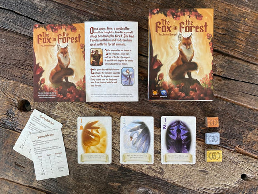 Card game components including cards and a box titled 'The Fox in the Forest' on a wooden surface.